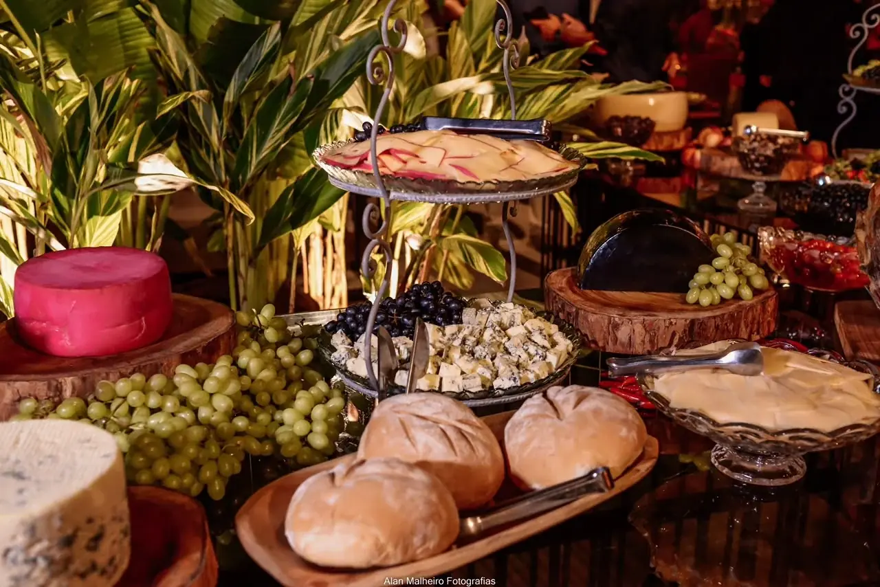 Mesa de frios com queijo, pães e uvas em primeiro plano.